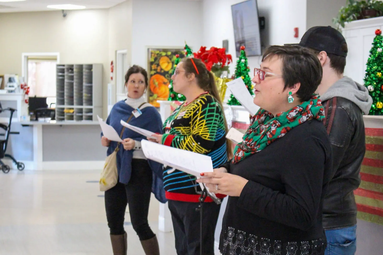 A group sings together at Hilltop, holding song sheets beside festive holiday decorations.