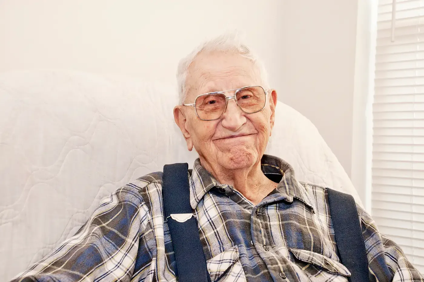 An older adult smiling warmly while seated at home, representing the individuals Hilltop’s Community Access Programs support by connecting them with benefits, caregiving resources, and local services that improve daily life.