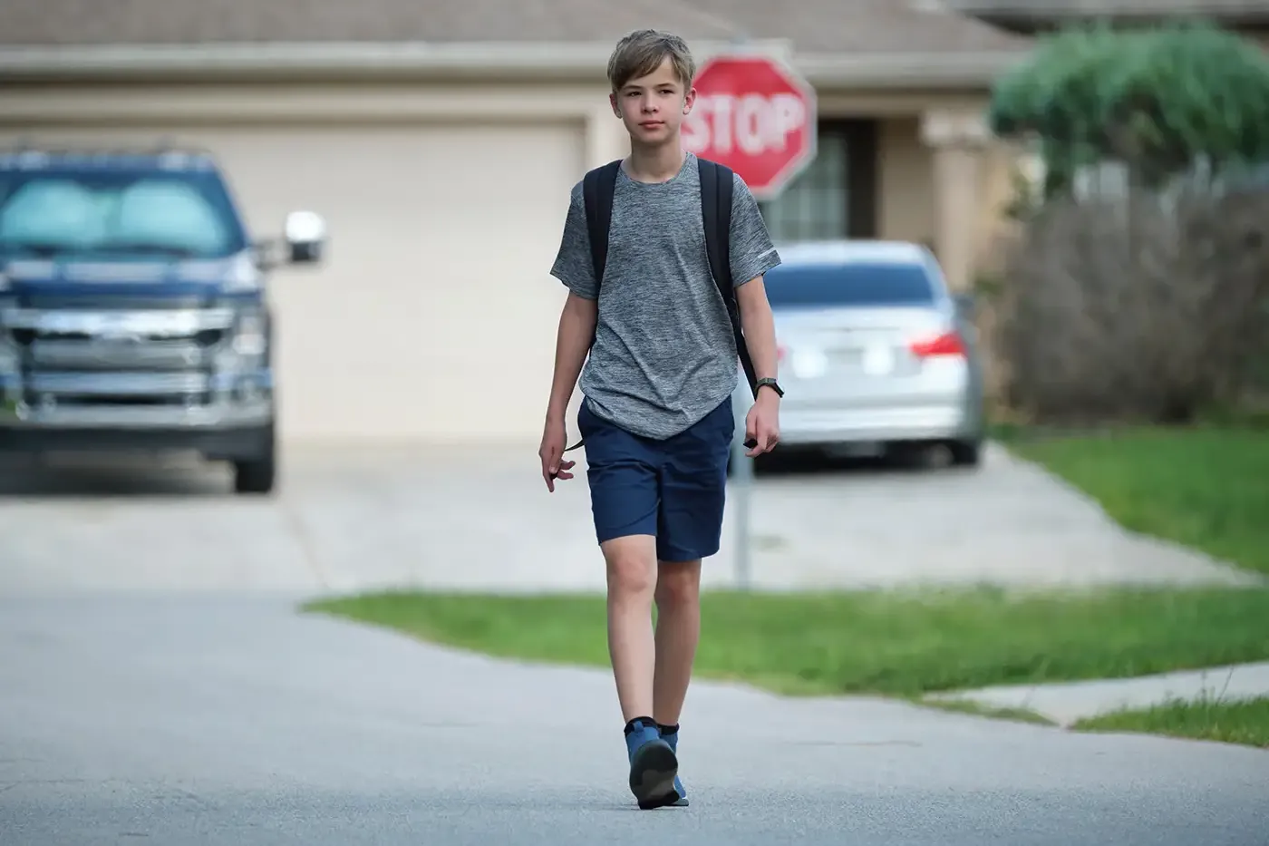 A teen walking through a neighborhood with a backpack, symbolizing the focus of Hilltop’s youth programs on keeping young people safe, connected to school and family, and supported with positive alternatives to detention.