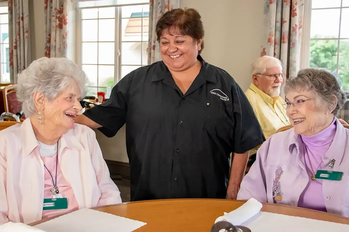 Residents at a Hilltop Senior Living community sharing a warm moment with a staff member, reflecting the welcoming environments, supportive care, and vibrant social connections offered at The Cottages, The Commons, and The Fountains of Hilltop.